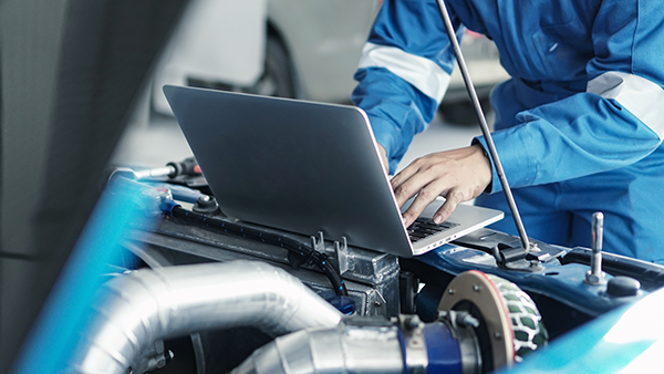 Mechanic using laptop sitting on a car engine
